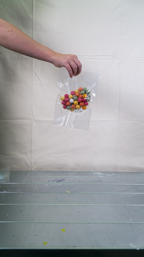A hand holding a plastic container filled with colorful round chewing gums.